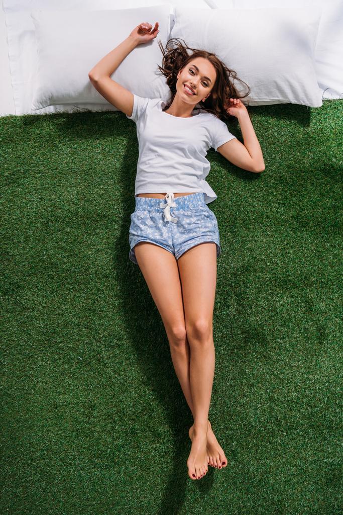 Młoda kobieta uśmiechający się na poduszki na zielony trawnik, ogólny widok - Zdjęcie, obraz