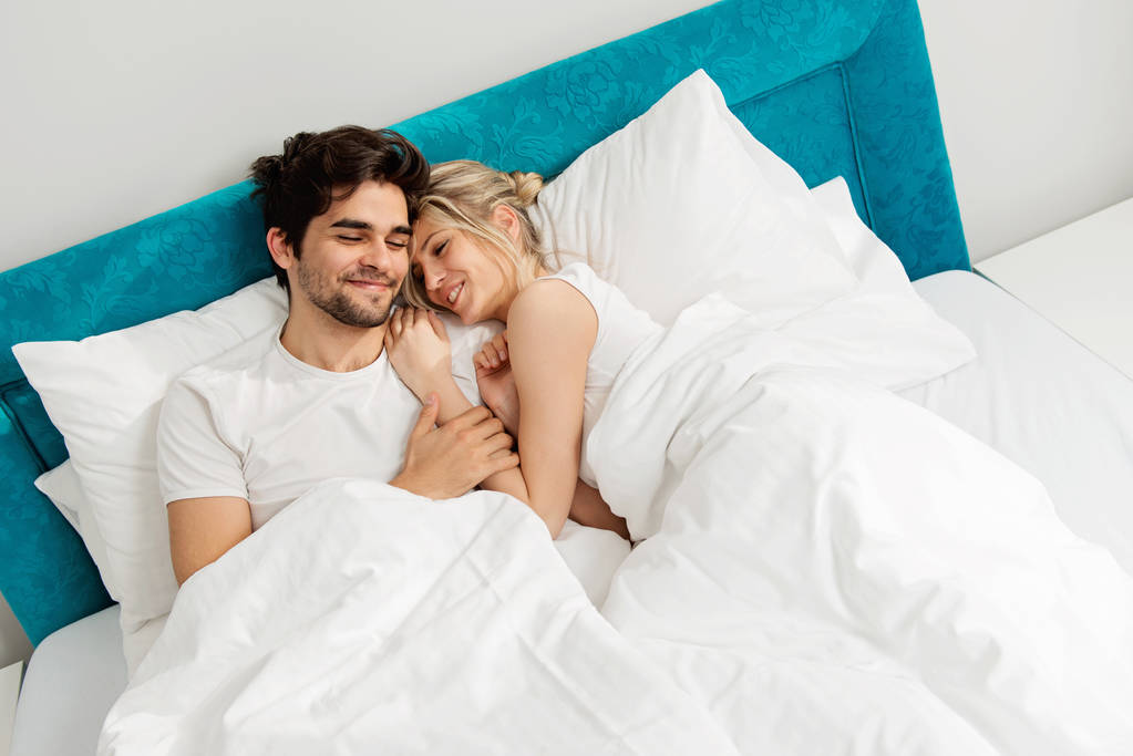 Νεαρό ερωτευμένο ζευγάρι ξαπλωμένο στο κρεβάτι, απολαμβάνοντας - Φωτογραφία, εικόνα