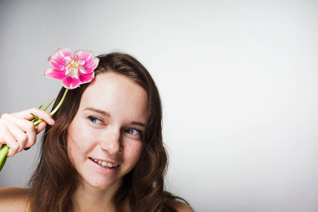 linda chica de ojos azules sonriendo, sosteniendo una flor rosa fragante
 - Foto, Imagen