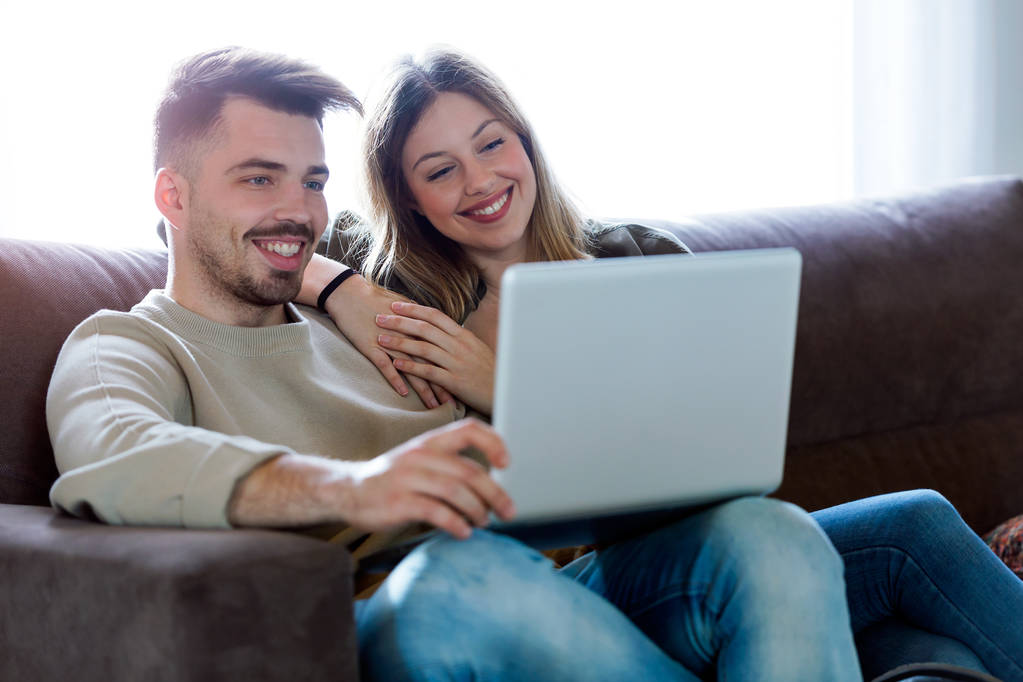 Beau jeune couple souriant en utilisant leur ordinateur portable à la maison
. - Photo, image