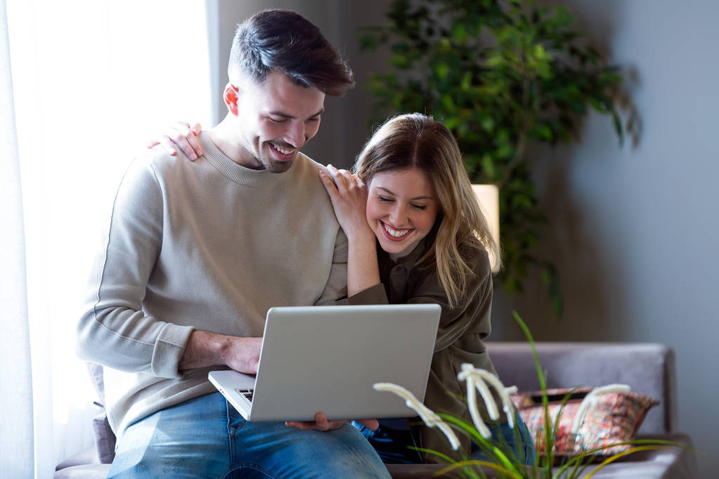 Kaunis nuori hymyilevä pari käyttävät kannettavaa tietokonetta kotona
. - Valokuva, kuva