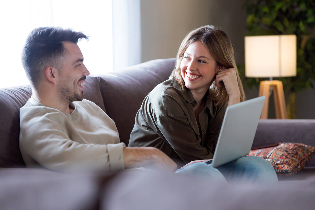 Beau jeune couple souriant en utilisant leur ordinateur portable à la maison
. - Photo, image