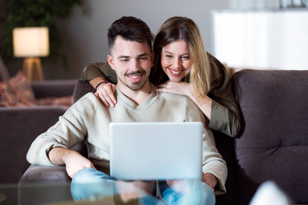 Красива молода усміхнена пара використовує свій ноутбук вдома
. - Фото, зображення