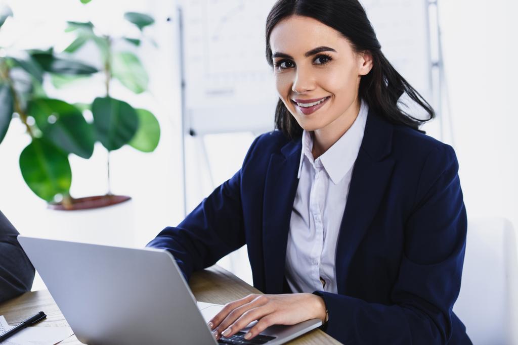 lächelnde attraktive Geschäftsfrau, die im Büro mit Laptop arbeitet - Foto, Bild