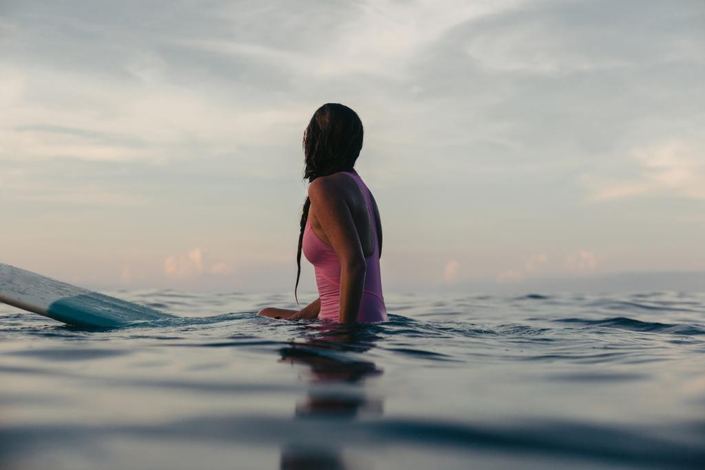 silhouette of female surfer sitting on surfboard in water at sunset - Photo, Image