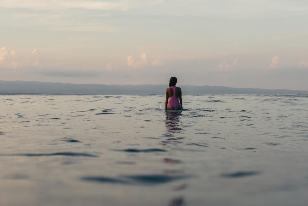 vue arrière de la silhouette d'une surfeuse assise sur une planche de surf dans l'eau
  - Photo, image