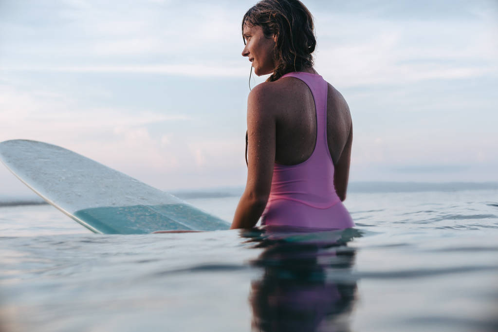atraktivní žena sedící na surfovací prkno v oceánu při západu slunce - Fotografie, Obrázek