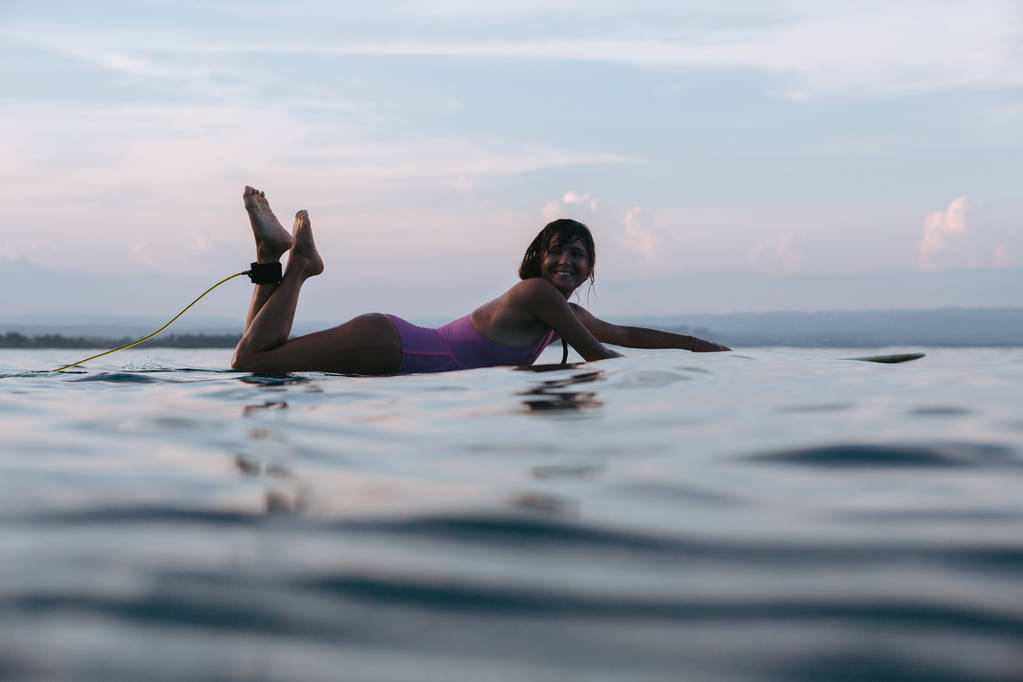 uśmiechnięta kobieta, leżąc na deski surfingowej w wody oceanu o zachodzie słońca - Zdjęcie, obraz