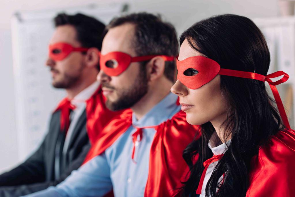 Zijaanzicht van super ondernemers in maskers en capes op zoek weg in kantoor - Foto, afbeelding