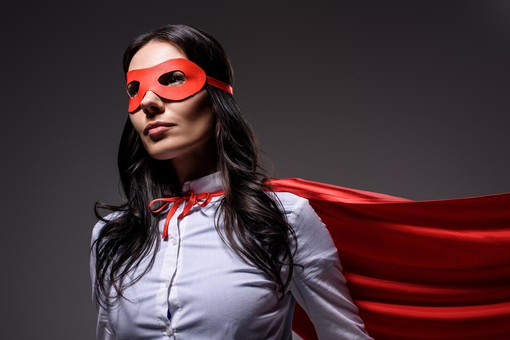 ελκυστική σούπερ επιχειρηματίας στην κόκκινη κάπα και μάσκα που απομονώνονται σε μαύρο - Φωτογραφία, εικόνα