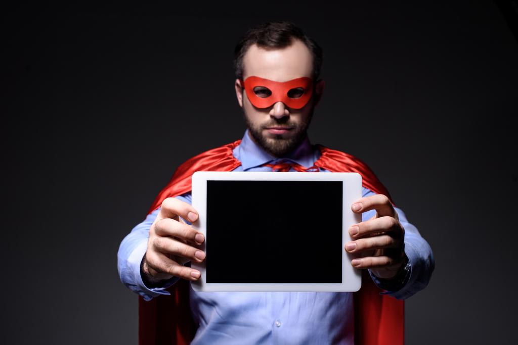 knappe super zakenman in masker en cape tonen tablet geïsoleerd op zwart - Foto, afbeelding