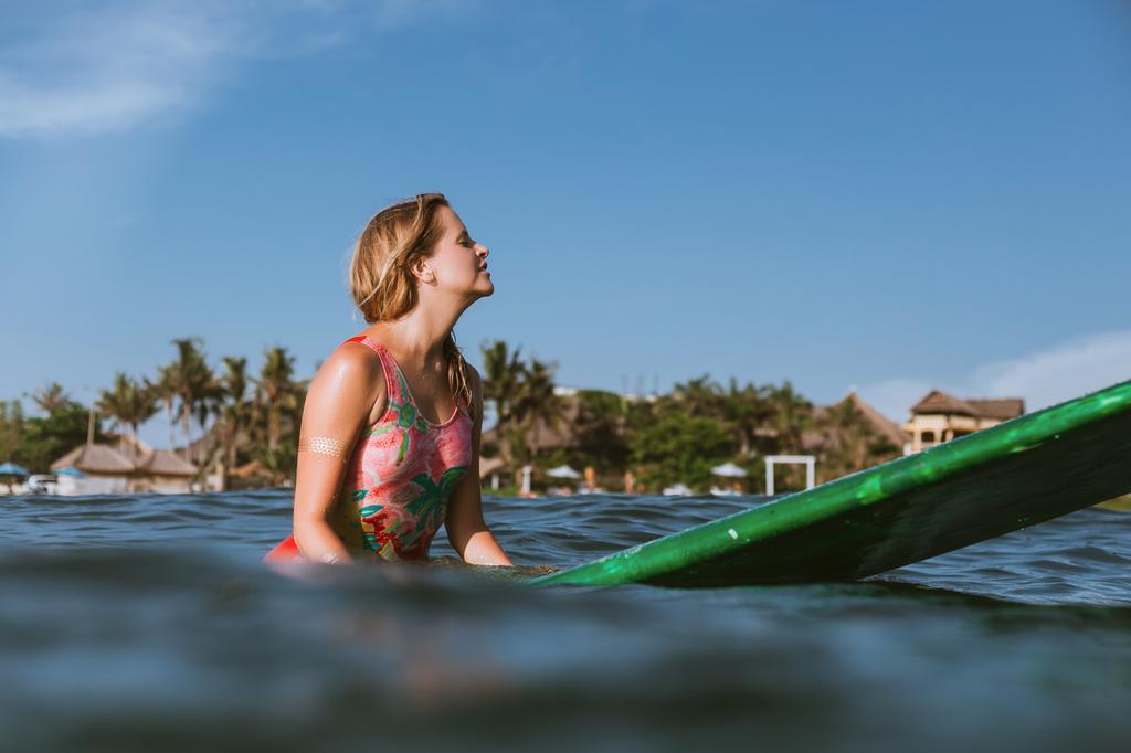 vista laterale della giovane donna in costume da bagno appoggiata su tavola da surf in oceano con costa sullo sfondo
 - Foto, immagini