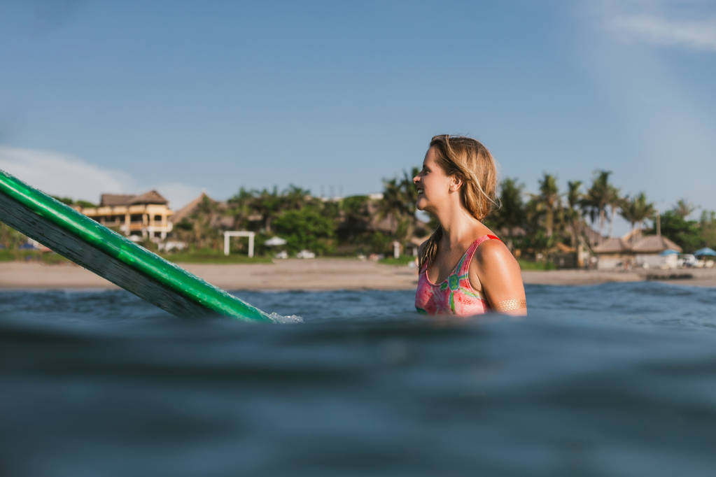 vue latérale de la jeune femme en maillot de bain reposant sur planche de surf dans l'océan avec le littoral sur le fond
 - Photo, image