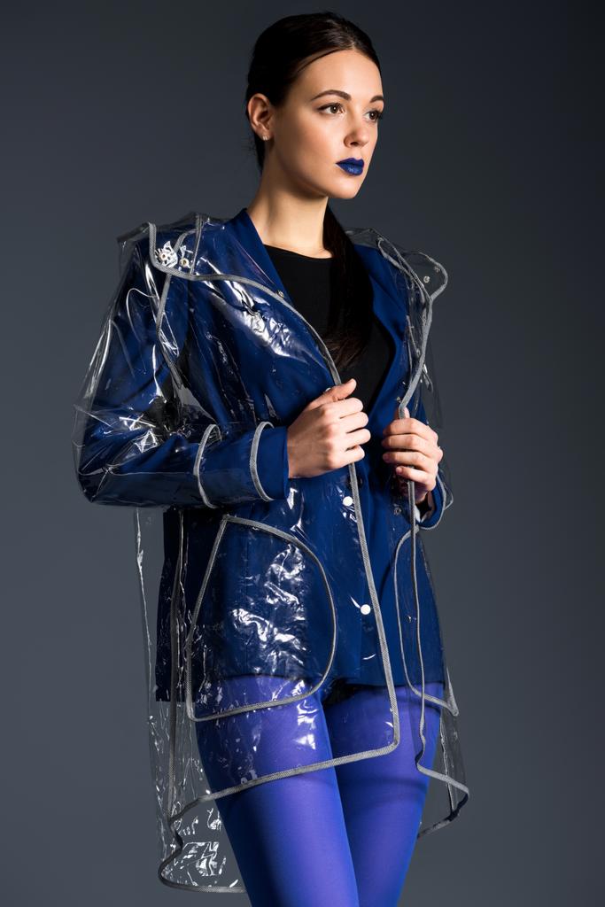 Brunette girl in blue jacket and raincoat isolated on dark background - Photo, Image