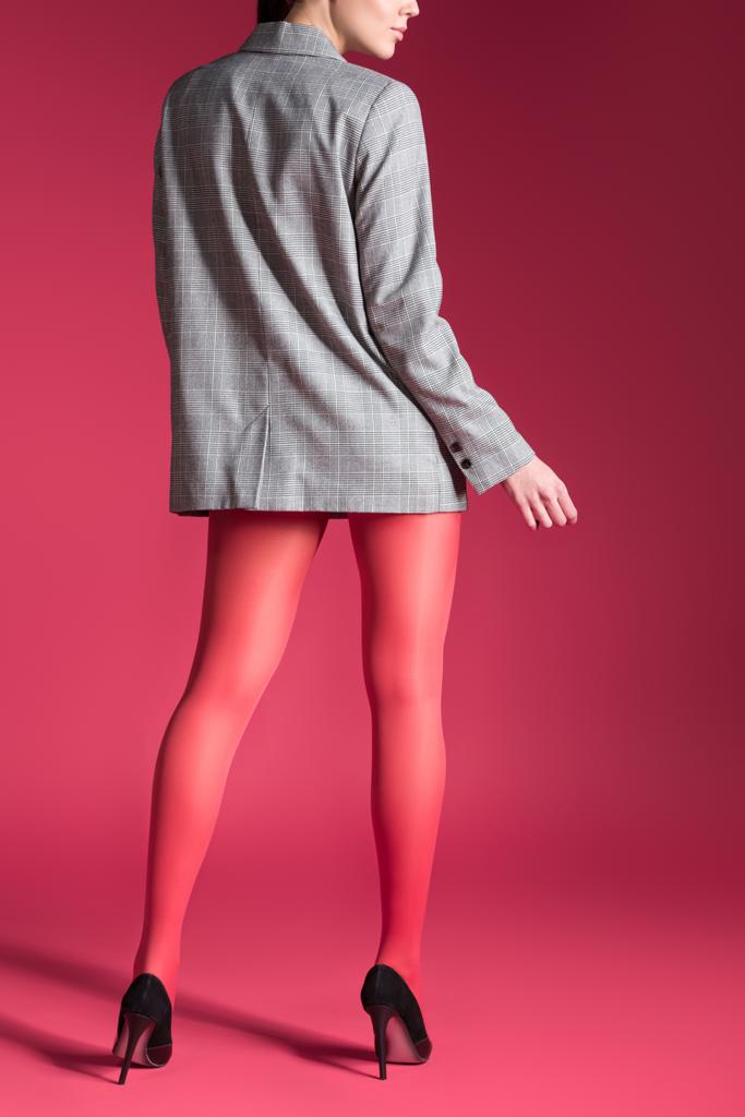Woman posing in red pantyhose and grey jacket on red background - Photo, Image