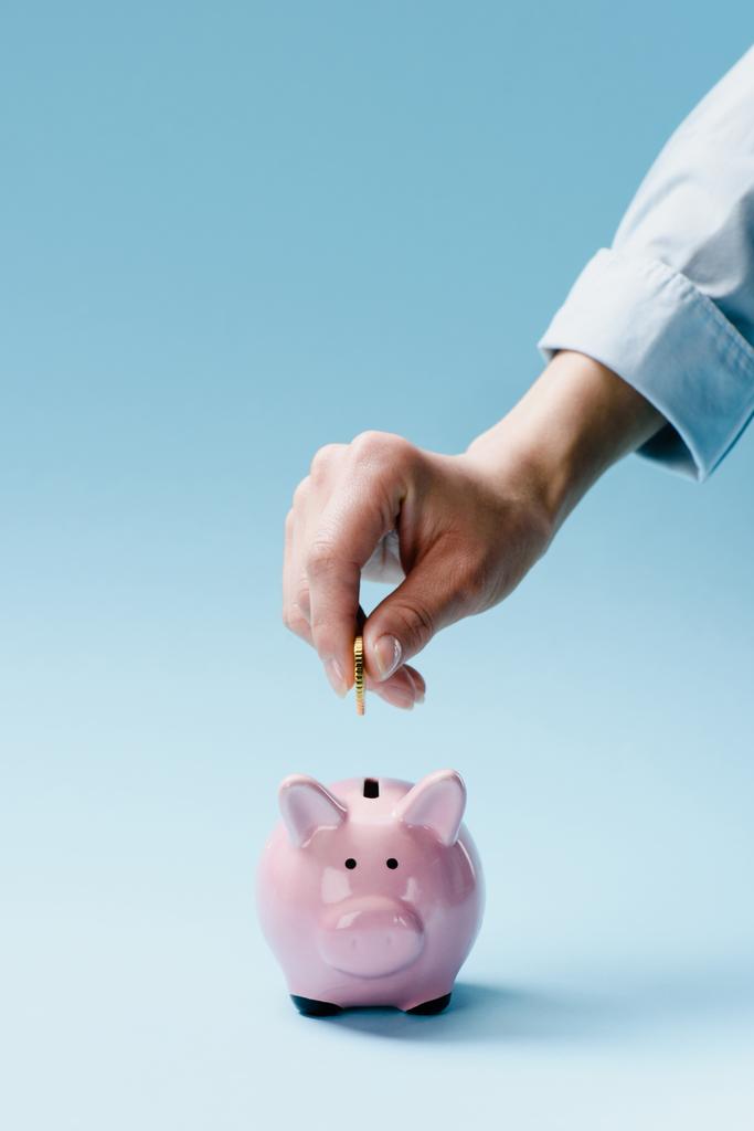 częściowy widok człowieka, wprowadzenie monet do pink piggy bank na niebieskim tle - Zdjęcie, obraz