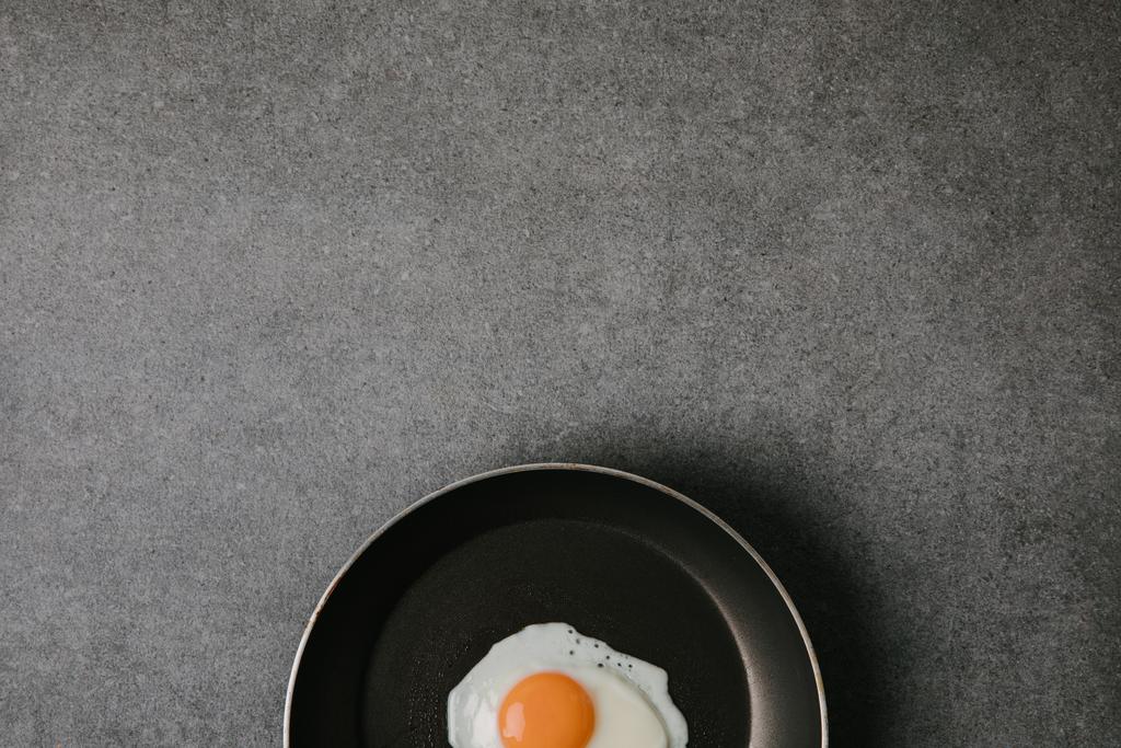 верхний вид сковородки с вкусным жареным яйцом на сером фоне
 - Фото, изображение