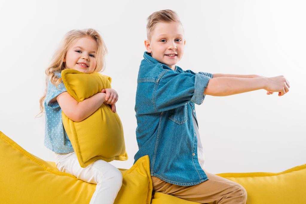 щасливий хлопчик прикидається водієм, сидячи на жовтому дивані з сестрою
 - Фото, зображення
