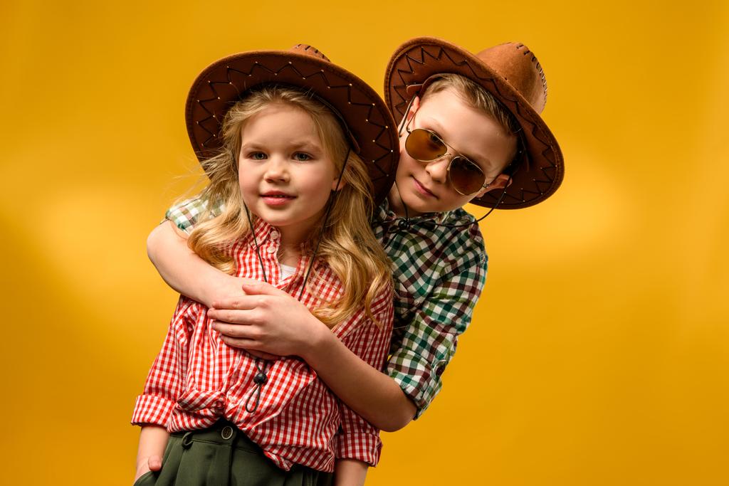 kleine stylische Cowboy und Cowgirl in Hüten umarmen isoliert auf gelb - Foto, Bild
