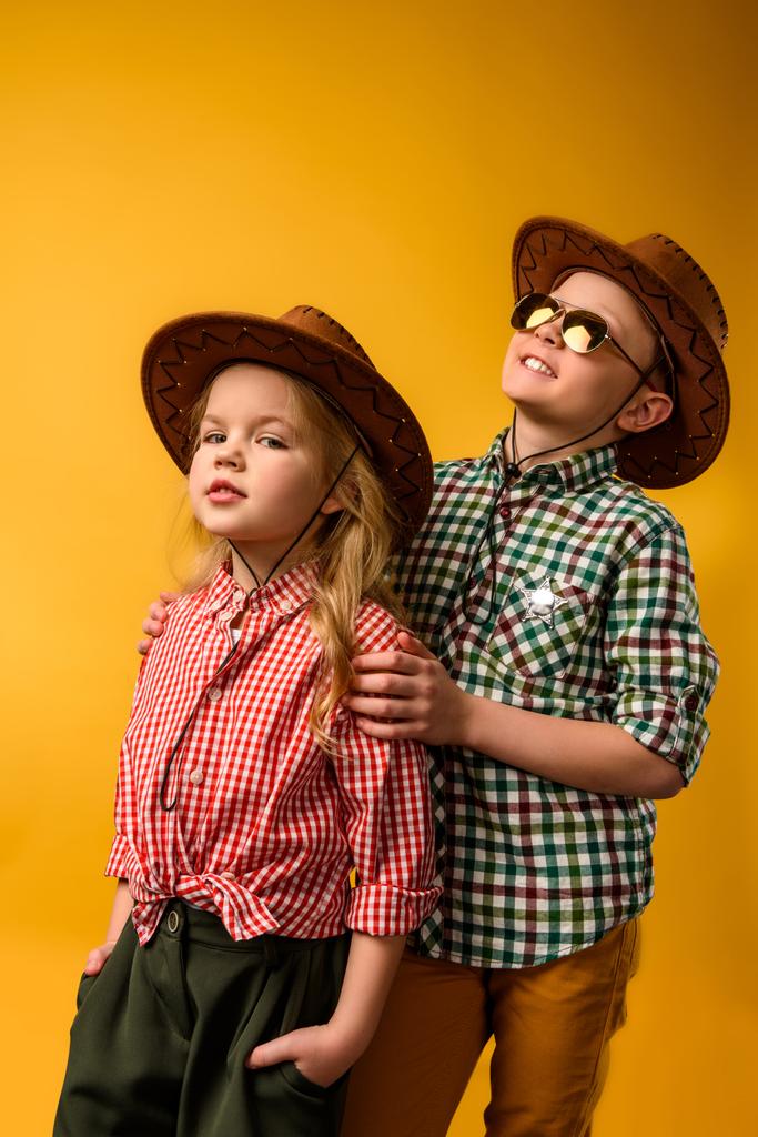 beetje stijlvolle cowboy en cowgirl in hoeden, geïsoleerd op geel - Foto, afbeelding