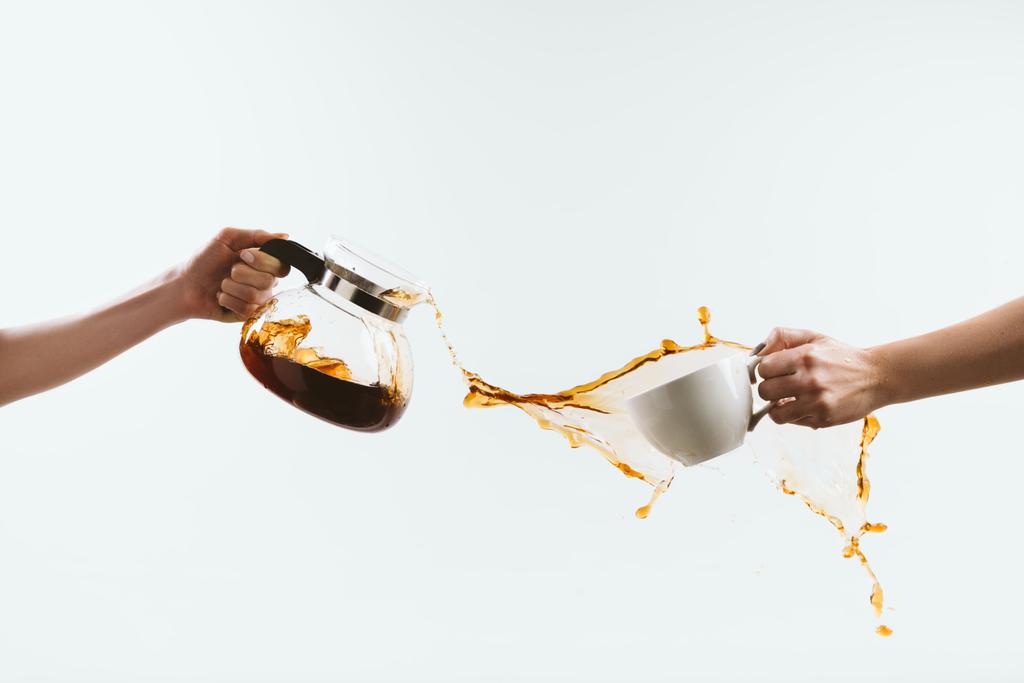 abgeschnittene Ansicht der Person, die Tasse und Glaskanne mit Kaffeespritzen hält, isoliert auf weiß - Foto, Bild