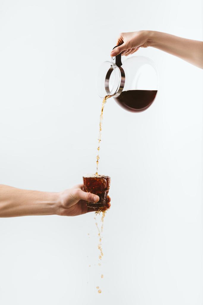 bijgesneden weergave van handen gieten koffie uit pot in glas, geïsoleerd op wit - Foto, afbeelding