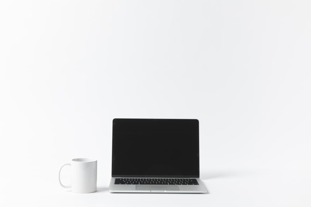 Close-up van laptop met leeg scherm en witte mok geïsoleerd op wit - Foto, afbeelding