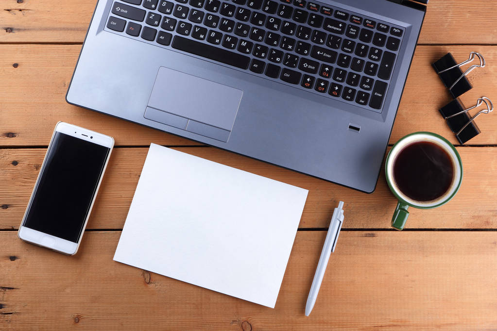 Laptop und Kaffeetasse auf hölzernem Hintergrund, Arbeitsplatz auf altem Schreibtisch, Smartphone und Notizbuch, Stift und Brille am Arbeitsplatz, Designerarbeitsplatz, Büro - Foto, Bild