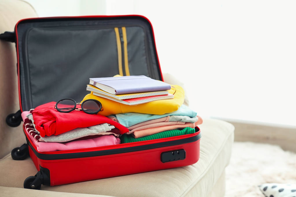 Reisekoffer mit Kleidung und Notizbüchern auf dem Sofa - Foto, Bild