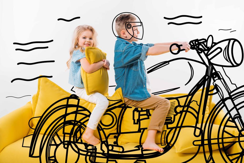 boy pretending to be a biker and riding motorbike while sitting on yellow sofa with sister - Photo, Image