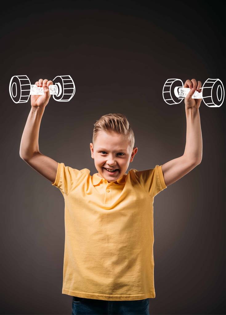 garotinho sorrindo fingindo ser um esportista e treinando com halteres, isolado em cinza
 - Foto, Imagem