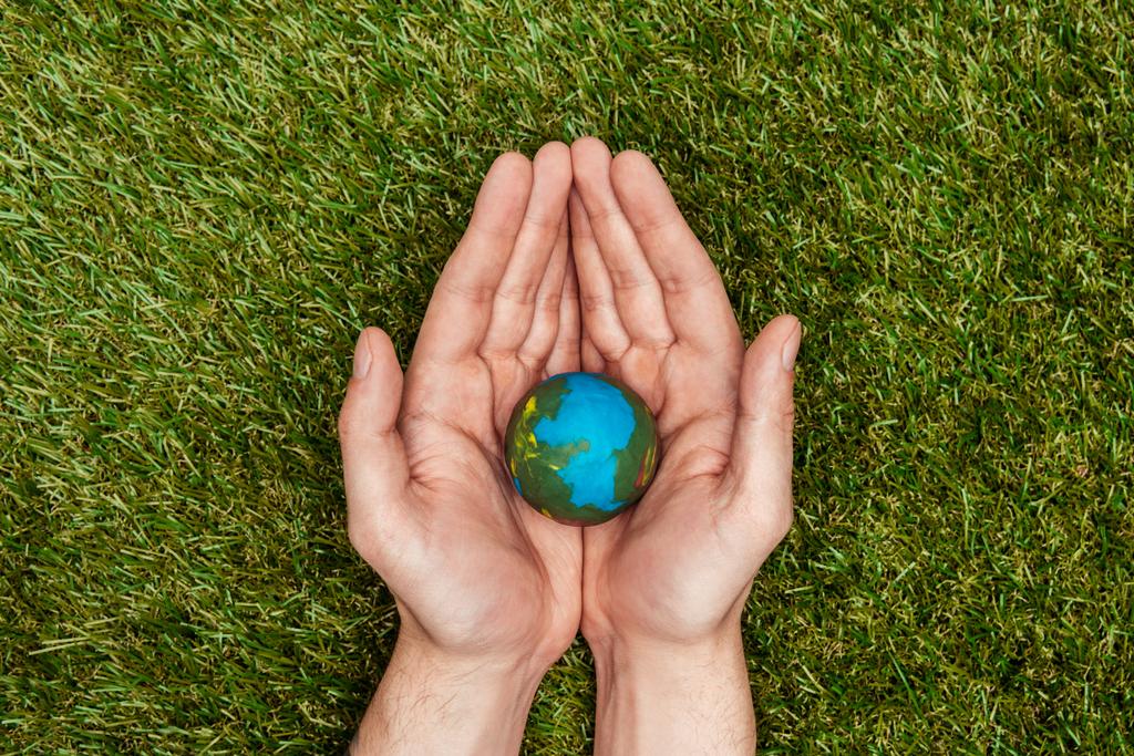 levágott kép ember tartja a föld modell kezében fölött zöld fű, föld napja koncepció - Fotó, kép