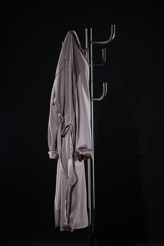 casaco de trincheira pendurado no rack do casaco isolado no preto
 - Foto, Imagem