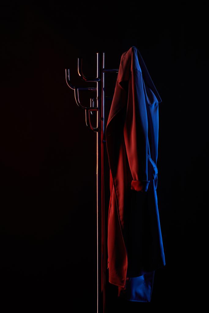 fogas, ruhaakasztó elszigetelt fekete tónusú fényben lóg kabát - Fotó, kép