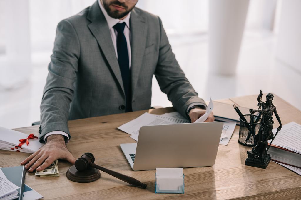 обрезанный снимок юриста, берущего взятку на рабочем месте с документами и ноутбуком в офисе
 - Фото, изображение