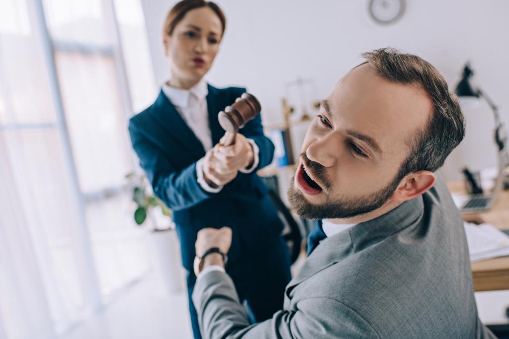 enfoque selectivo de abogado fingiendo golpear a colega con mazo en las manos en la oficina
 - Foto, Imagen