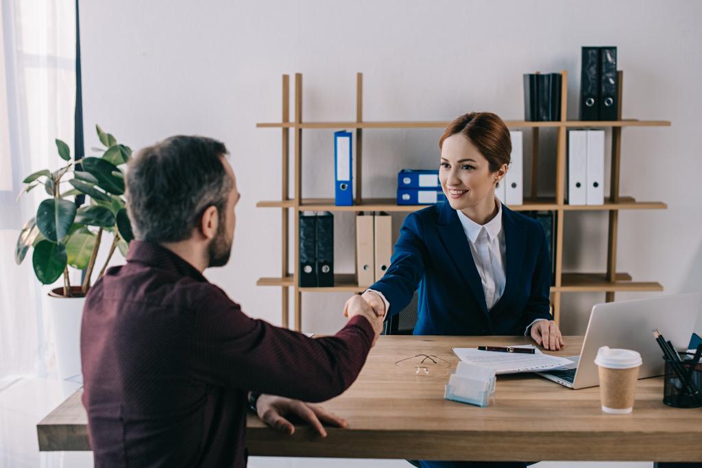 улыбающаяся деловая женщина и клиент пожимают руку на встрече в офисе
 - Фото, изображение