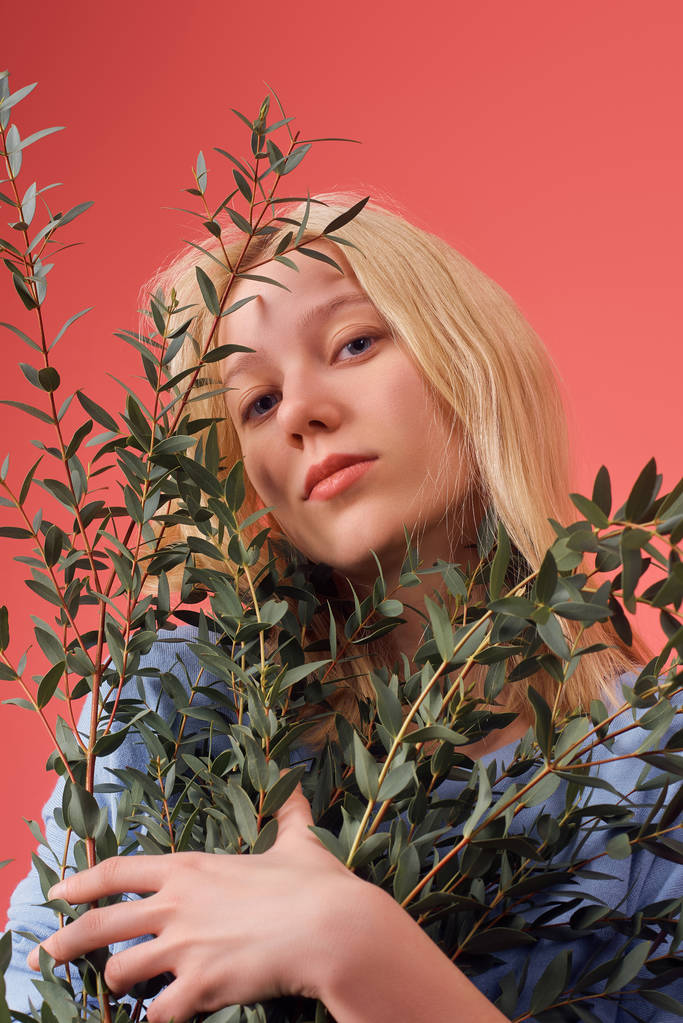 привлекательная молодая женщина с кучей эвкалиптовых ветвей, изолированных на красном
 - Фото, изображение