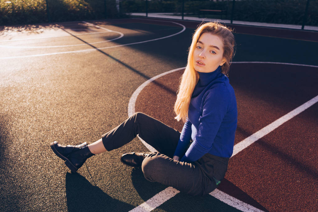 stylowy model Młoda Blondynka w Sweter niebieski pozowanie na boisko sportowe w słońcu - Zdjęcie, obraz