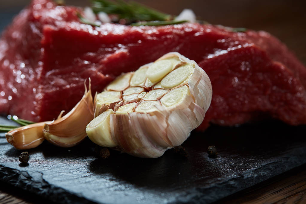 Çiğ et dana biftek siyah üzerine kurulu baharat, sarımsak ve biberiye ile ahşap arka plan üzerinde seçici odak kayrak - Fotoğraf, Görsel