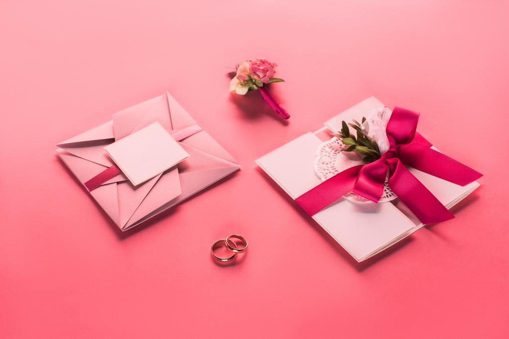 wedding rings, boutonniere and pink envelopes with invitations on pink surface - Photo, Image
