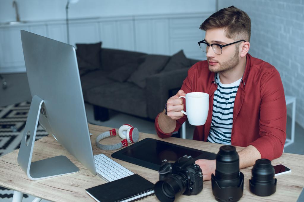 Молодой дизайнер работает за компьютером и пьет кофе
 - Фото, изображение