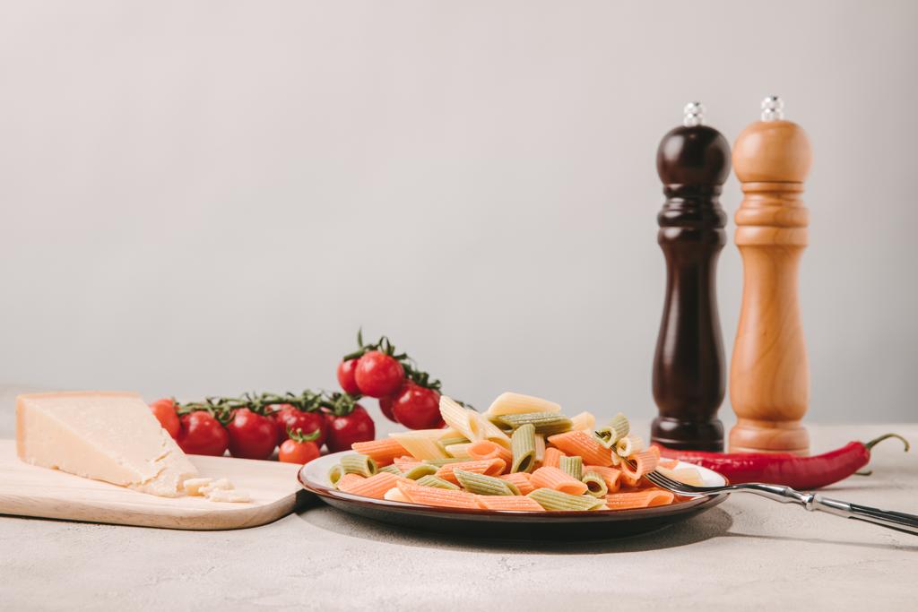 barevné těstoviny na talíř s rajčaty, sýrem a kořením na betonový podklad - Fotografie, Obrázek