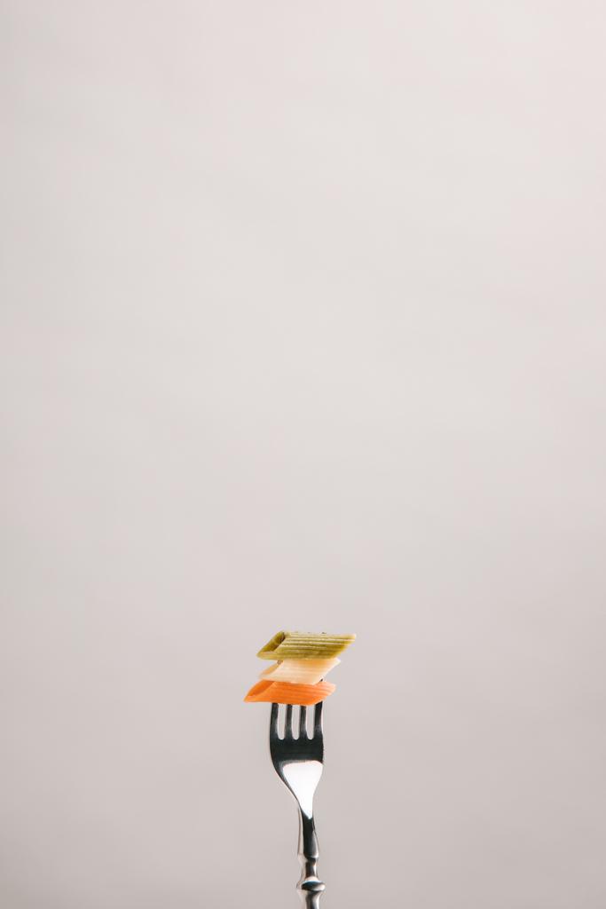 pasta colorata forata con forchetta isolata su grigio
 - Foto, immagini