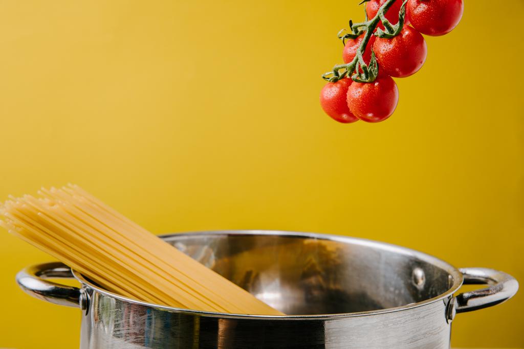 spaghetti bouillant dans une casserole avec branche de tomates cerises au-dessus isolé sur jaune
 - Photo, image