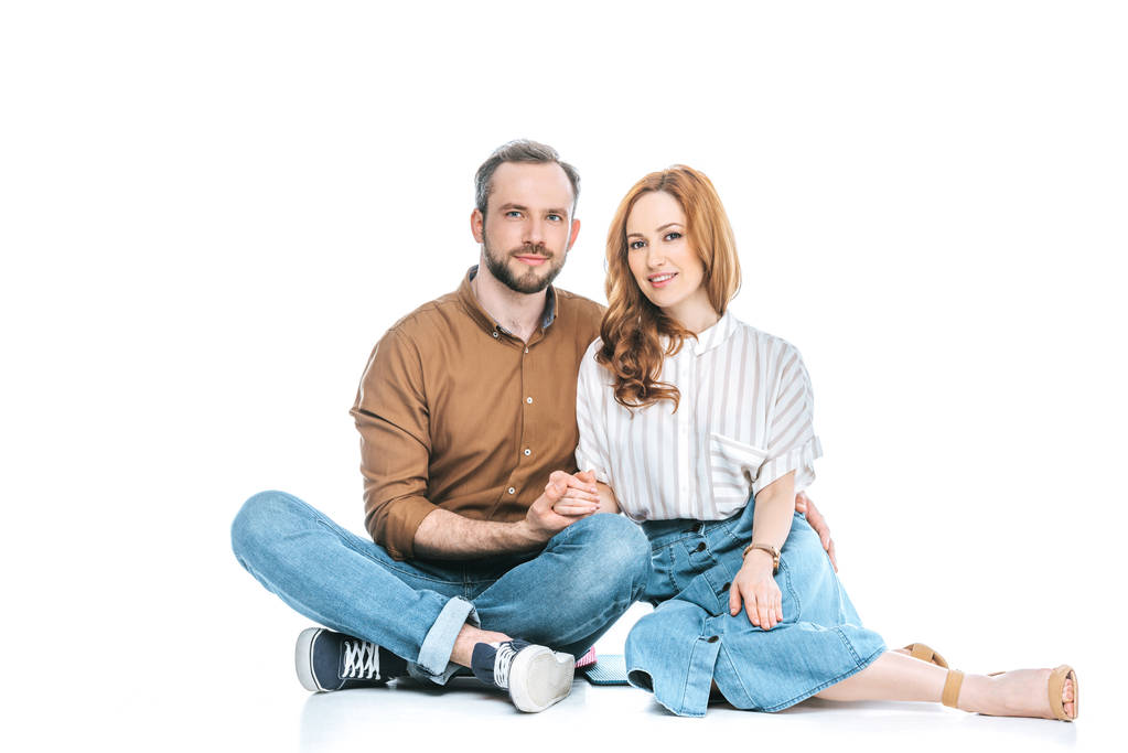 kaunis onnellinen pari istuu yhdessä, kädestä pitäen ja hymyillen kameralle eristettynä valkoisella
 - Valokuva, kuva