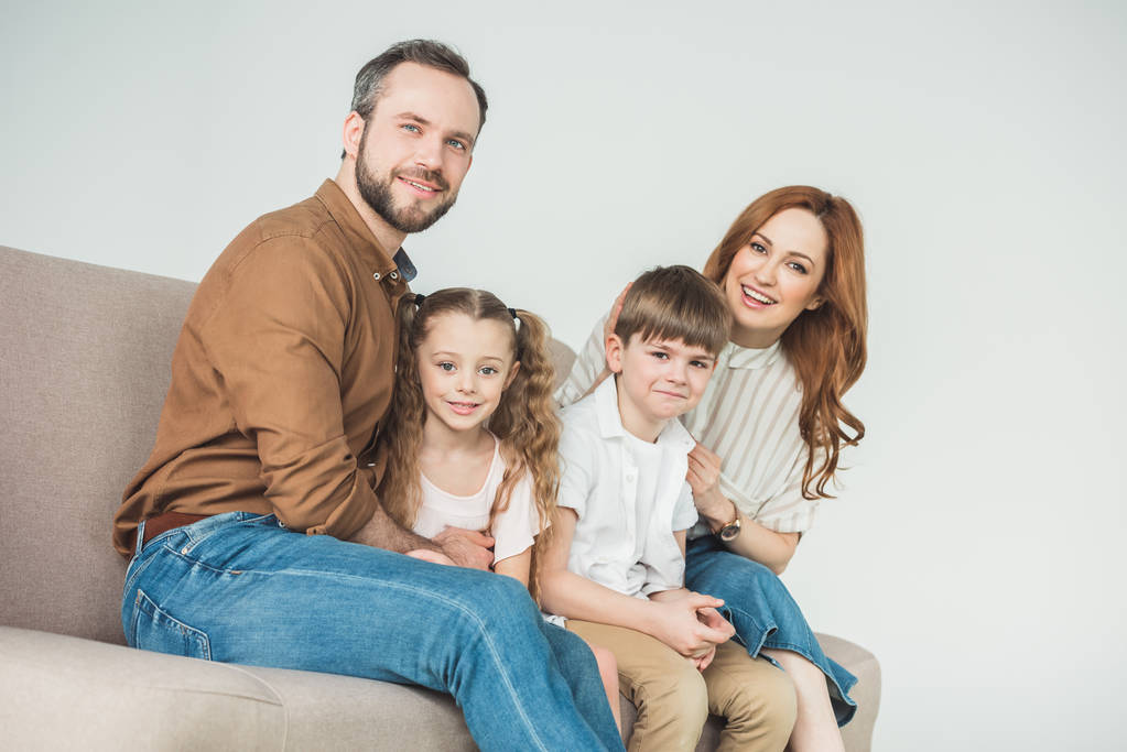 cheerful family with two children sitting on couch and smiling at camera on grey  - Photo, Image