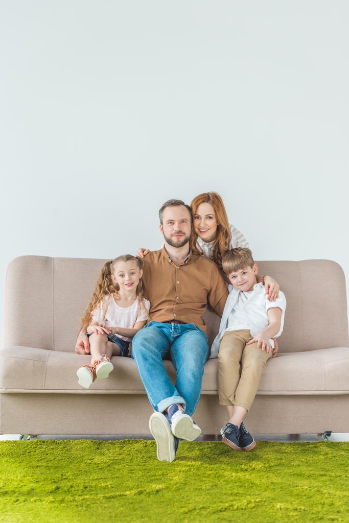 ομορφη ευτυχισμένη οικογένεια με δύο παιδιά, κάθεται στον καναπέ και να χαμογελά στη φωτογραφική μηχανή σε γκρι - Φωτογραφία, εικόνα