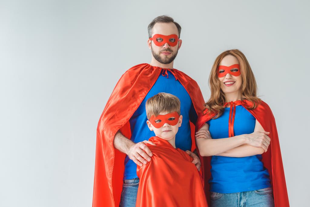 family of superheroes in masks and cloaks looking at camera isolated on grey - Photo, Image