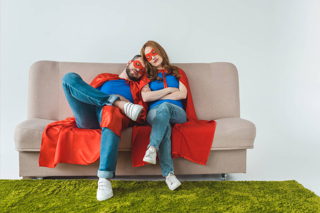 Müdes Paar in Superheldenkostümen schläft auf Sofa in Grau - Foto, Bild